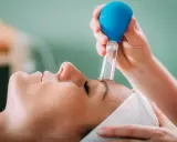 Zabieg z użyciem baniek na zatoki. Terapeuta delikatnie przykłada bańkę do czoła pacjentki, przynosząc ulgę.
