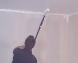 Person målar om taket med en lång roller.