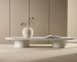 Ett minimalistiskt, coolt soffbord i vitt med en rund vas med torkade blommor och en öppen bok.