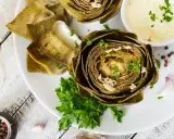 Deliciosas alcachofas al horno, tiernas y doradas, servidas con una cremosa salsa y perejil fresco. Un plato perfecto para disfrutar.