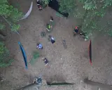 Ludzie rozbijają obóz w lesie, stosując zasady "leave no trace". Widać hamaki, plecaki i namiot.