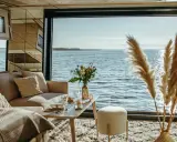 Przytulny salon z widokiem na wodę, idealny na nietypowe noclegi w Polsce. Sofa, stolik z kwiatami i puszysty dywan tworzą atmosferę relaksu.