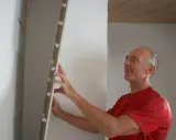 Man tapetserar på gipsskiva med ett leende.