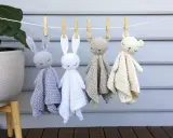 Cuatro adorables mantas de apego crochet, con forma de conejitos y ositos, cuelgan de una cuerda.