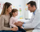 Medico esamina addome bambina con madre, preoccupati per possibile tumore di Wilms.