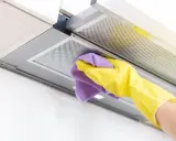 Mano con guante amarillo y paño morado limpiando la campana extractora por dentro.