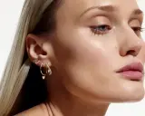 Delikatne kolczyki z kwiatami i serduszkiem, zdobiące ucho modelki, dodają subtelnego blasku.