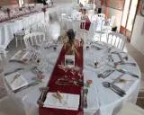 Une table dressée à la française, prête pour un événement. Nappes blanches, chemins de table bordeaux, vaisselle et couverts élégants, et une touche champêtre avec des épis de blé et de la lavande.