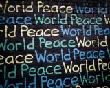 Un promemoria di Gianni Rodari: "Pace nel mondo" scritto in giallo, blu e verde su un muro di mattoni neri.