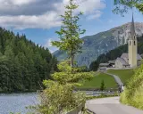 Passeggiata sul lago di Valdurna, con boschi rigogliosi, una chiesa alpina e montagne sullo sfondo.