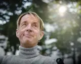 En leende man med rullstol, kanske en scen från filmer med Nils Hallberg, tittar upp mot solen.
