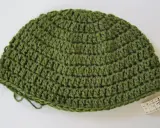 Gorro de lana verde tejido a mano, ideal para aprender como tejer un gorro de lana para principiantes. Cinta métrica al lado.