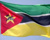 Flaga Mozambiku: zielono-czarno-białe pasy, czerwony trójkąt z żółtą gwiazdą, karabin AK-47 i książka.