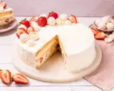 Eine köstliche Erdbeer Raffaello Torte, verziert mit frischen Erdbeeren und Kokosraspeln. Ein Stück ist bereits angeschnitten.
