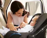 Madre abrochando el cinturón de seguridad a su bebé en la silla del coche. Los niños en el coche viajan seguros.