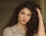 Une jeune femme aux longs cheveux frisés, portant de grandes créoles dorées. Sa coupe de cheveux frisés met en valeur son visage.