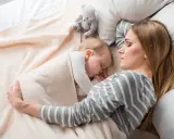 Mamma e bimbo dormono abbracciati, un tenero momento di co sleeping con un orsetto di peluche.