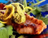 Grillad havsabborre med en grön topping och citronskal, serverad på en bädd av gröna blad.