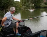 Mężczyzna siedzi nad wodą, trzymając długą wędkę. Pokazuje, jak zrobić wędkę, przygotowując się do łowienia.