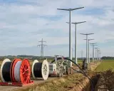 Kabeltrommeln und Bagger im Feld, während neue Windräder aufgestellt werden. Die Energiewende Herausforderungen bei der Infrastruktur sind sichtbar.
