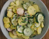 Kartoffelsalat mit Schale, garniert mit Radieschen, Gurken und Schnittlauch. Ein herzhaftes Gericht, das an Omas Küche erinnert.