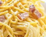 Cremige Spaghetti Carbonara, nur mit Eigelb zubereitet, garniert mit Speckwürfeln und schwarzem Pfeffer.