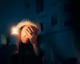 Kobieta w czapce trzyma świecę, zasłaniając twarz. To skutki przerwania dostaw energii elektrycznej do urządzeń o kluczowym znaczeniu.
