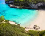 Traumhafte mallorca buchten mit türkisfarbenem Wasser, weißem Sand und grünen Pinien. Ein Boot ankert im Meer, eine Rettungsschwimmerturmbefindet sich am Strand.