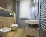 Bagno moderno con bidet, WC sospeso, lavabo e scaldasalviette cromato. L'illuminazione a LED sotto il marmo crea un'atmosfera elegante, rispettando l'altezza minima soffitto.
