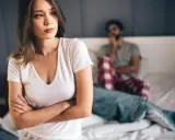 Kobieta zmartwiona, mężczyzna w tle. Problemy intymne, może uczulenie na spermę?