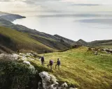 Trzech turystów podczas trekkingu na zielonym wzgórzu z widokiem na morze i góry.