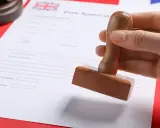 Dłoń trzymająca pieczątkę nad dokumentem wizowym z flagą Wielkiej Brytanii.