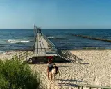 Sianożęty atrakcje: drewniane molo wchodzi w morze, plaża i fale.