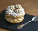 Un délicieux Paris-Brest saupoudré de sucre glace, prêt à être dégusté avec une cuillère.