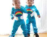 Två små tvillingar i glittriga blå dräkter med regnbågar och moln. De ser ut att vara redo för ett äventyr!