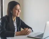 Uśmiechnięta kobieta w słuchawkach prowadzi wideokonferencję, pracując nad projektem sd worx.