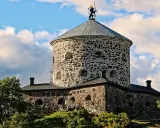 Skansen Lejonet, ett stendäckat torn med en gyllene lejonstaty på toppen, reser sig mot en molnig himmel.
