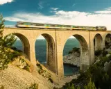 Ein Zug rast über eine Bogenbrücke, die Teil des Bahnnetz Frankreichs ist. Das Meer glitzert unter den Bögen.