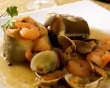 Delicioso abadejo a la donostiarra con gambas y almejas en una salsa dorada, adornado con perejil fresco.