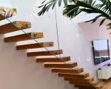 Escalera flotante de madera con **rejas de cristal** que aportan ligereza y modernidad al espacio.