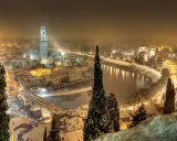 Verona innevata, un'incantevole **città da visitare a dicembre**. La neve copre i tetti e il fiume Adige riflette le luci della città.