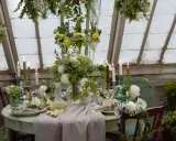 Vacker blomsterdekoration på bordet med levande ljus och gröna detaljer. En inbjudande dukning i ett växthus.