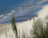Plaża z falami, piaskiem i kilkoma spacerującymi osobami, widok z klifu.
