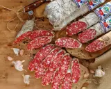 Eine Auswahl an italienischen Salami-Sorten, aufgeschnitten und im Ganzen, mit Knoblauch und Pfefferkörnern auf Holz.