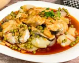 Merluza a la gallega con patatas, guisantes y ajo frito en una salsa rojiza.