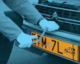 Ręce w białych rękawiczkach montują żółtą tablicę rejestracyjną z symbolem starego auta. Czy warto zarejestrować auto jako zabytek?