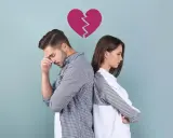 Para stojąca plecami do siebie, z pękniętym sercem nad głowami. Smutek i dystans symbolizują trudne życie po zdradzie.