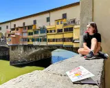 Ragazza seduta sul Ponte Vecchio, con la guida "Firenze cosa vedere in due giorni" a fianco.