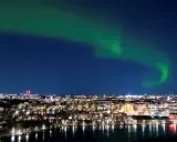 Grön norrsken dansar över ett upplyst Stockholm vid vatten.