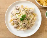 Szybki obiad z makaronem farfalle w kremowym sosie grzybowym, posypany natką pietruszki. Idealny na szybki posiłek.